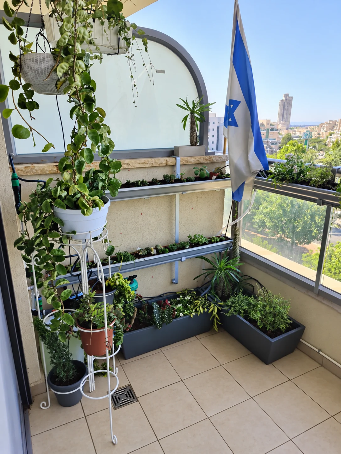 אדניות תלויות ועציצים במגוון גבהים סביב פינת המרפסת.